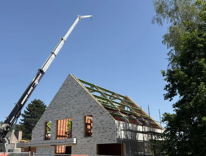 Houten dakconstructie wordt met de kraan op een nieuwbouw geplaatst