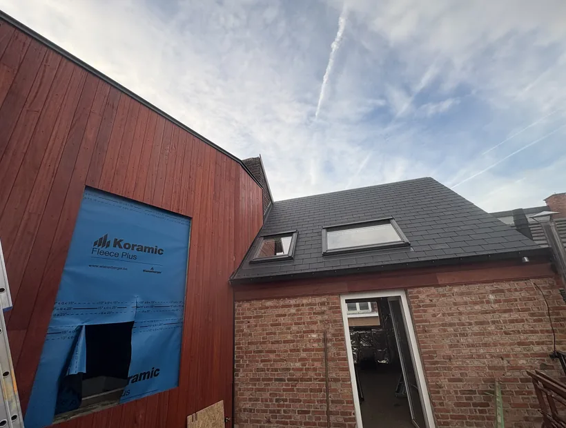 Gevelbekleding in hardhout naast een leien dak met dakraam